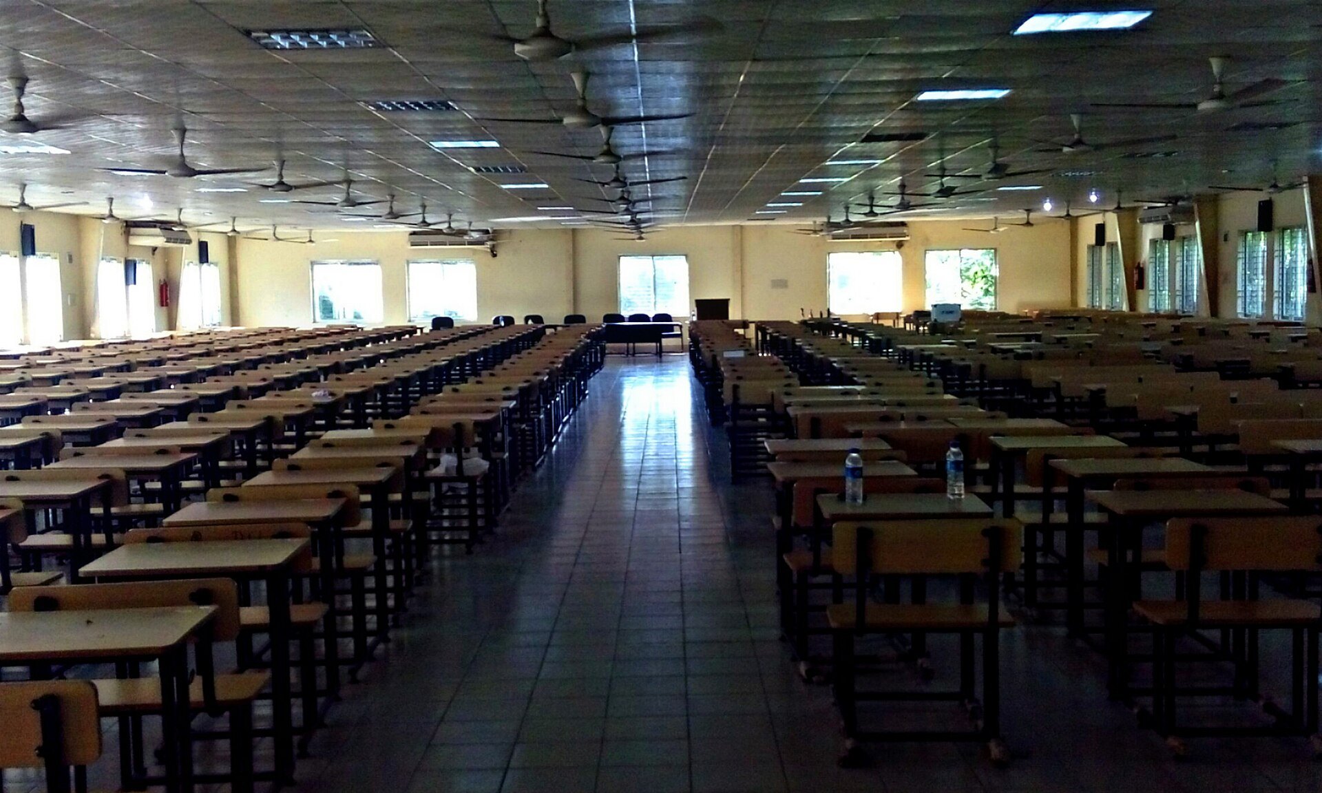 Rows of empty wooden desks set up for an exam in a large hall