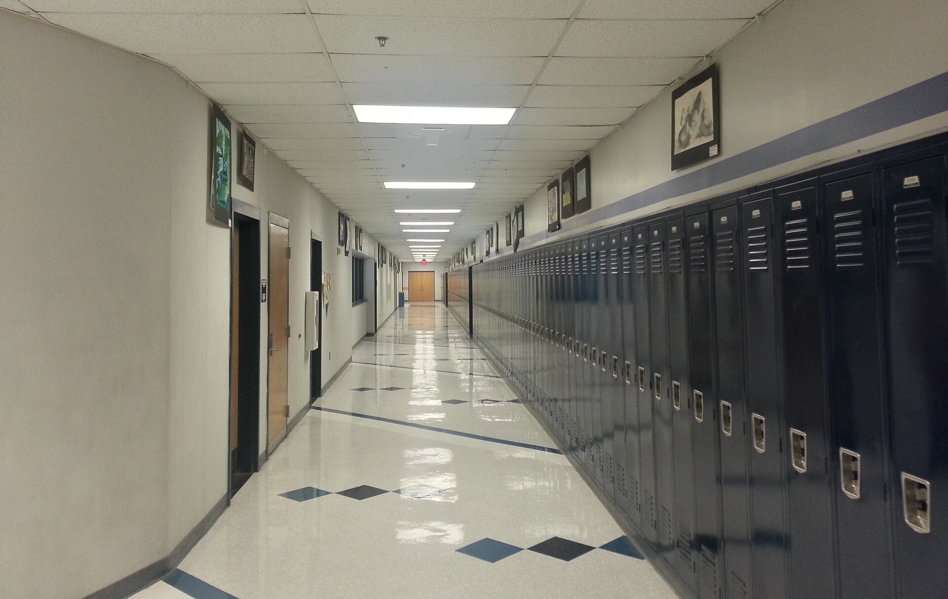 Long high school hallway lined with dark blue lockers and a polished tile floor