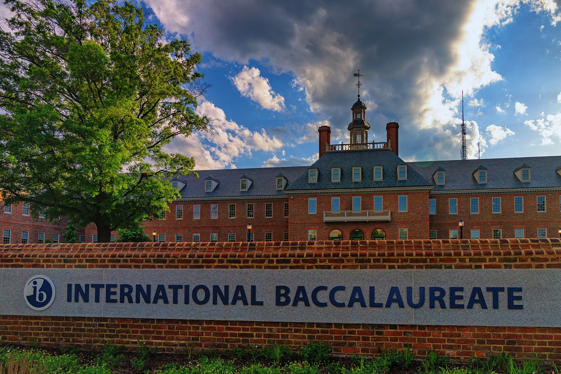 International Baccalaureate sign on a brick wall in front of a red brick building with a white cupola